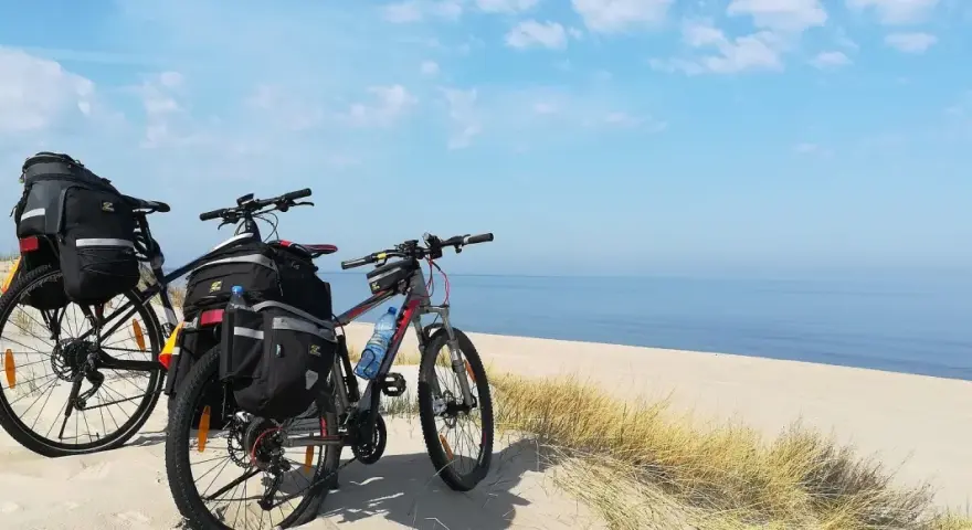 Dwa rowery z sakwami na plaży, gotowe na przygodę wzdłuż Velo Baltica. Morze i niebo tworzą tło.