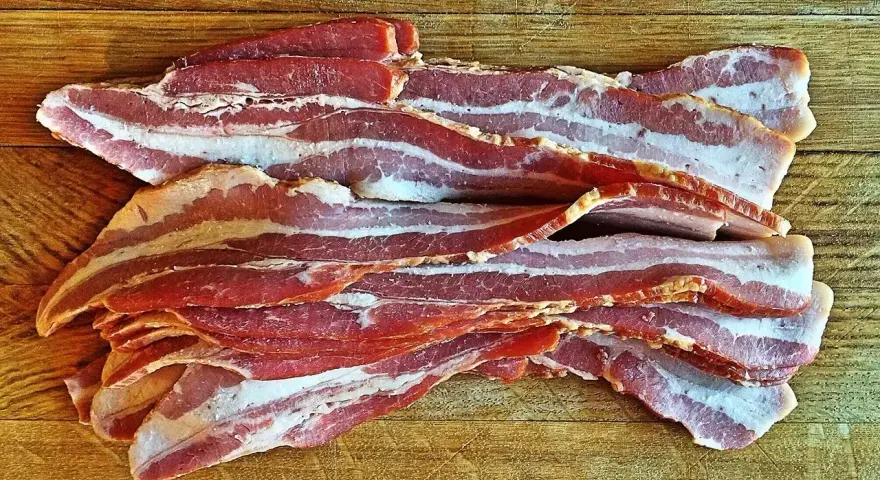 Surowy boczek ułożony na drewnianej desce. Idealny do chrupiącego smażenia, ale pamiętaj o jego kaloryczności - boczek kcal.