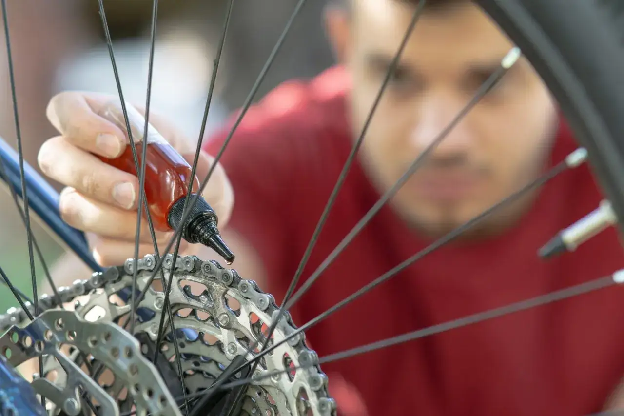 Mężczyzna aplikuje smar do łańcucha rowerowego, dbając o płynną jazdę. Pytanie: czym smarować łańcuch rowerowy? Odpowiedź widać na zdjęciu.