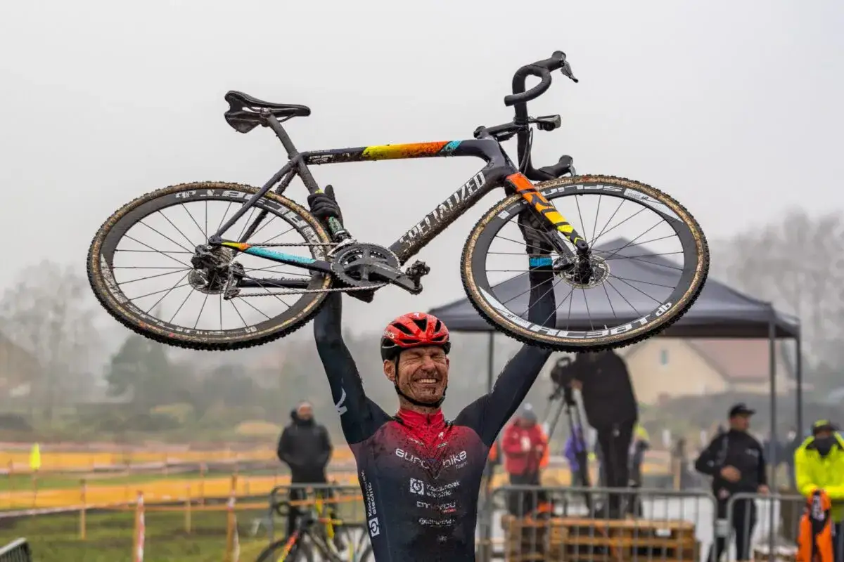 Szczęśliwy zwycięzca zawodów rowerowych podnosi swój brudny rower nad głowę.