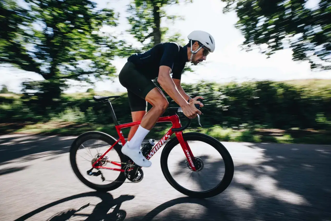 Mężczyzna w kasku i stroju kolarskim podczas intensywnego treningu cardio na rowerze szosowym.