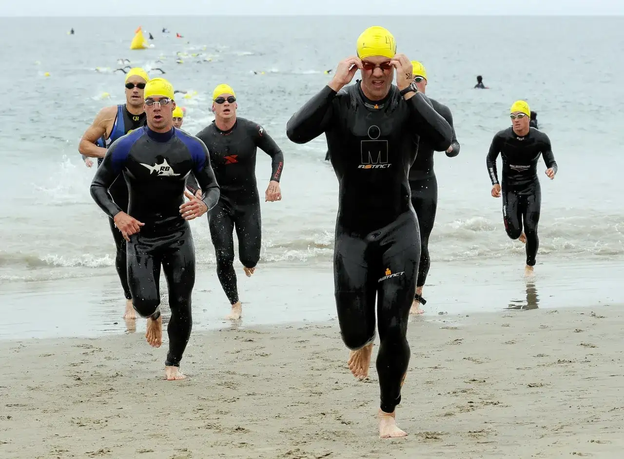 Zawodnicy w strojach do triathlonu biegną plażą do wody. Długi triathlon dystans to wyzwanie.