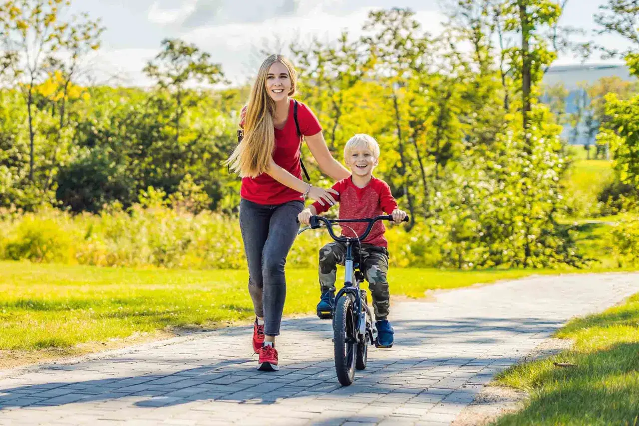 Mama uczy synka, jak nauczyć dziecko jeździć na rowerze. Radosny chłopiec na rowerze, mama biegnie obok.