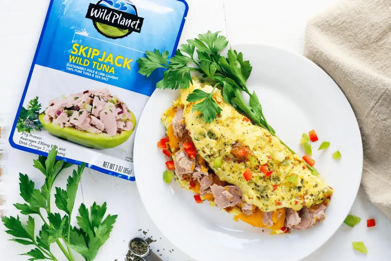 Omlet z tuńczykiem, kolorowy i apetyczny, z dodatkiem papryki i ziół, obok opakowania tuńczyka Wild Planet.