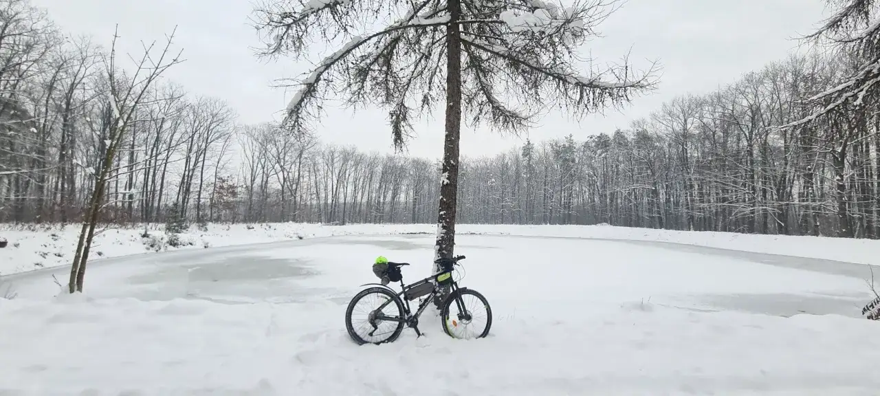 Rower do kolarstwa gravelowego czeka na przygodę nad zamarzniętym jeziorem w zimowym lesie.