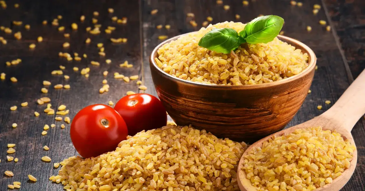 Miseczka pełna kaszy bulgur, obok pomidorki i drewniana łyżka. Zdrowa kasza bulgur kcal to świetny wybór.